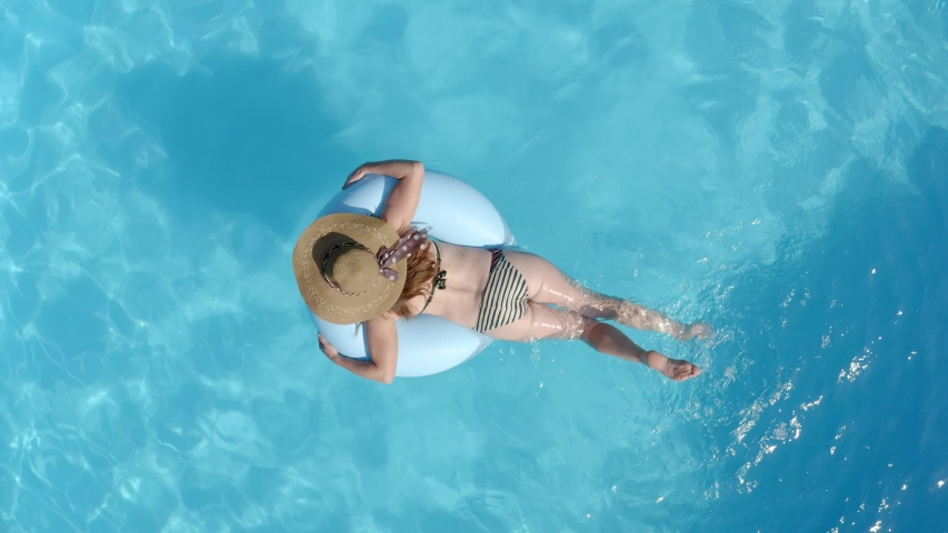 Top view of woman in bikini swimming in pool lying on inflatable mattress. | Shutterstock HD Video #1031164979