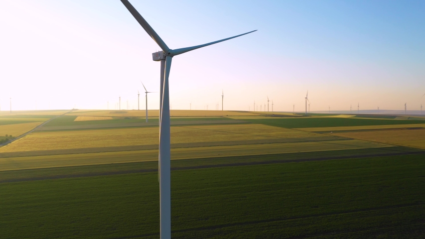 Aerial view of Wind turbines Energy Production- 4K aerial shot on sunrise. Wind energy farm. Eolian generators in a beautiful wheat field. Eolian turbine farm. Wind turbine silhouette. Windmill farm. Royalty-Free Stock Footage #1031166329