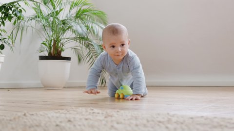 Curious Baby Boy Playing With Toys On Floor At Home Crawls Towards And Looks At Camera