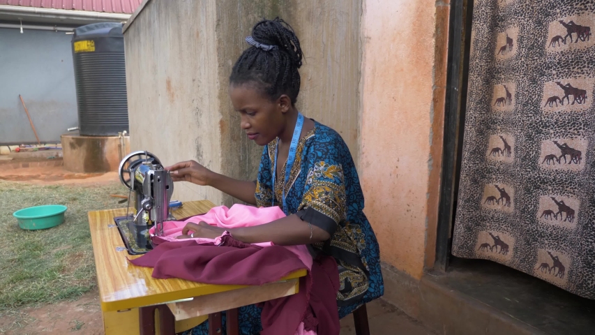 Side view in slow motion of an African lady sewing clothes on a manual tailoring machine outside her small house. | Shutterstock HD Video #1031168327