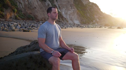 A strong young man in silhouette sitting in a meditation pose to release stress and train mindfulness and positivity at sunrise in Santa Barbara, California SLOW MOTION.