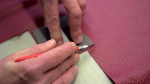A sharp industrial man knife cuts a piece of red leather. Italian Artigiano creates parts of a leather bag on a work desk. The hands of the artist. Tools and workplace in the industry