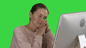 Blonde girl with pink pullover looking at monitor of computer watching video on a Green Screen, Chroma Key.