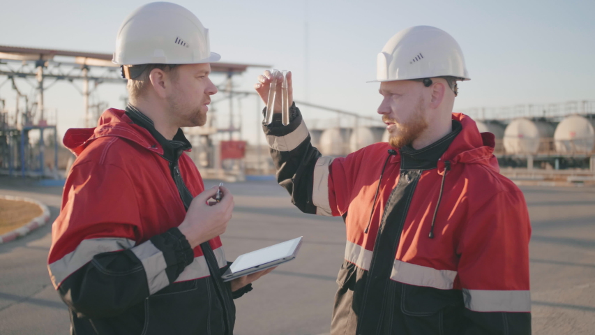 Half length portrait of two petrochemical engineers in helmets and uniform that examine two test tubes with oil and compare with requirements on tablet screen Royalty-Free Stock Footage #1031178602