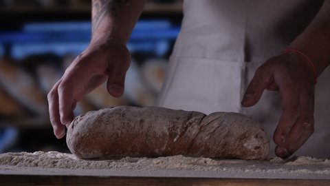 In the bakery, the hands of the baker are seen very closely as he prepares various flour products in an apron, after which he lays on the shelf. Concept of: Fresh Bread, Pizza, Bakery, Slow Motion.	