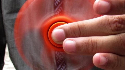 Close up of hands of a young Caucasian boy playing with orange colored Fidget spinner.