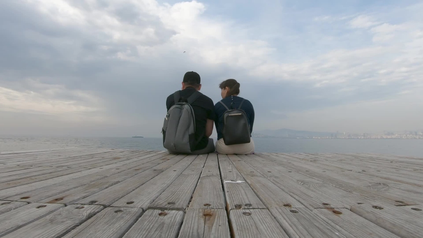 A couple in love sitting on a wooden pier and cute talking, admiring the sea view. beautiful timelapse