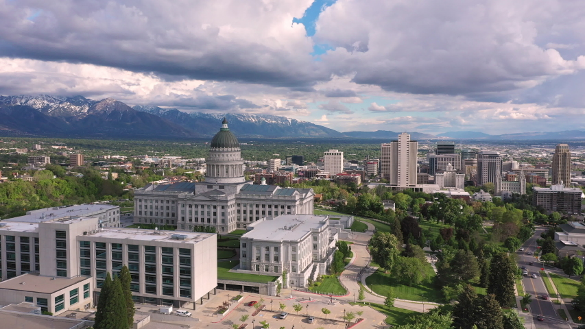 Wide panning aerial view of Salt Lake City and traffic driving next to the Capitol on cloudy day looking towards the Wasatch Mountains.