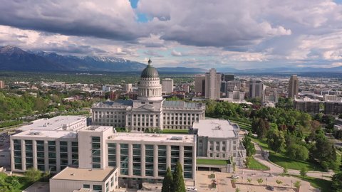 Aerial view flying past the Capitol building towards Downtown Salt Lake City, Utah with fluffy clouds in the sky.