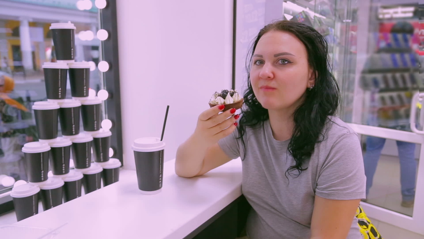 A brunette woman in a cafe is eating a cake with coffee