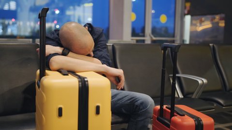 A man sleeping leaning on the yellow suitcase in the airport lounge. The delay of the flight.