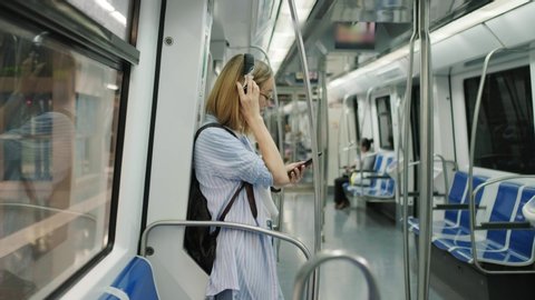 Young modern girl rides the subway and listens to music in headphones using a smartphone. Student rides the subway. Underground. Metro Barcelona