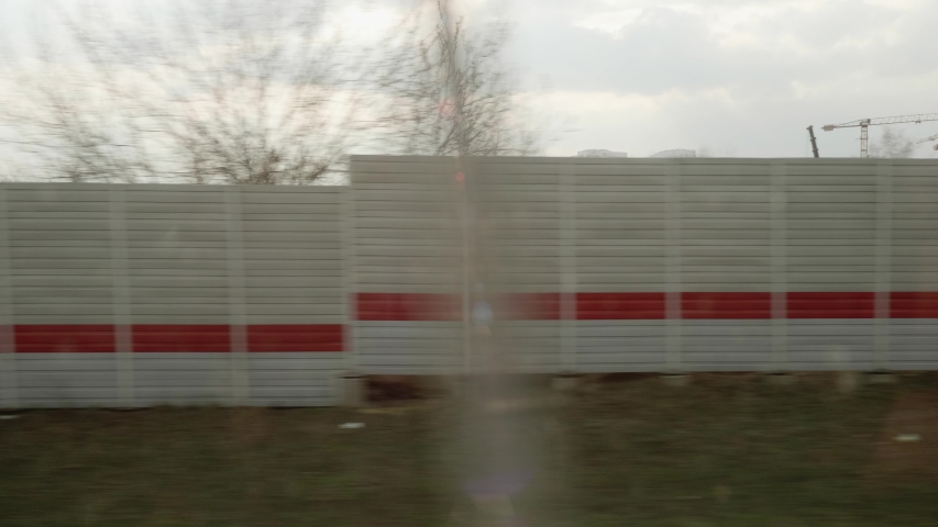 View of fence and industrial area from window of moving train.