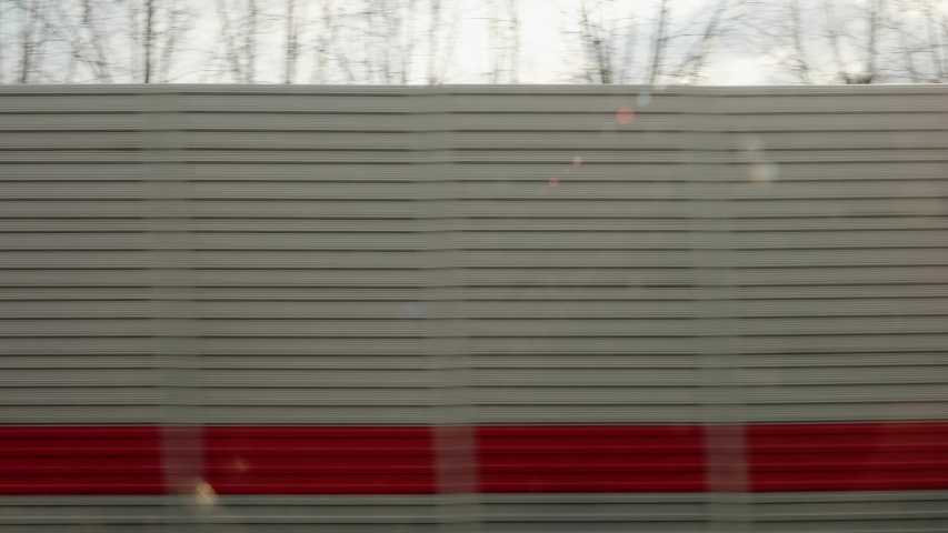 View of grey and red fence. View from window of moving train. Soundproofing fence