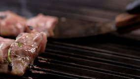 Chef moving pieces of marinated surgeons with metallic spatula on hot surface of barbecue grill, moving slider camera slow motion video close up slices of fish, cooking process