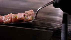 Chef cooking slices of fish, man wearing black gloves holding metallic spatula putting pieces of marinated surgeons on hot surface of barbecue grill, moving camera slow motion video close up man hand