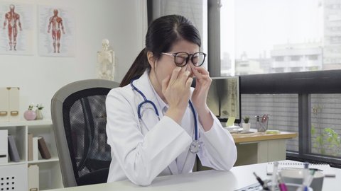 frowning woman doctor working on computer in clinic office feeling discomfort eye strain after long wearing glasses. medical nurse massaging nose bridge blurry irritated dry eyes eyesight problems.