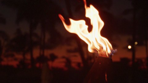 Torch with fire and flames burning in Hawaii sunset sky by palm trees. Beautiful slow motion torches on Hawaiian Waikiki beach, Oahu. RED EPIC SLOW MOTION