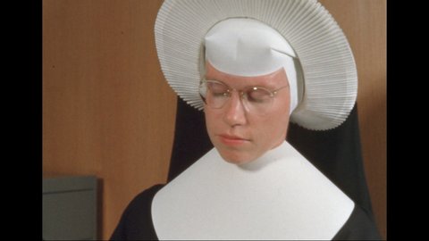 1960s: UNITED STATES: nurse looks at files in cabinet. Side view of nun's face.