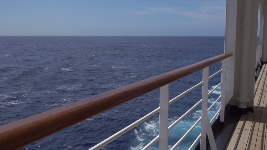 Slow pan from sea to railing and deck of cruise ship on sunny day at sea