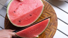 Female hand cutting watermelon fruit with a knife on wooden board. Selective focus.
