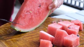 Female hand cutting watermelon fruit with a knife on wooden board. Selective focus.
