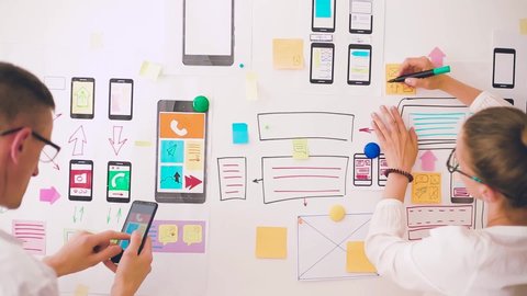 Designers is developing a web application for mobile phones. Woman draws a mockup of interface to smartphone. User experience.