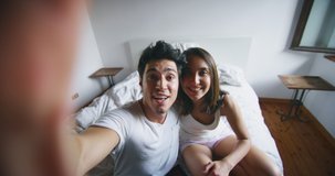 Slow motion of young just married couple are making a selfie or video call to relatives or friends with smartphone in the bedroom in the early morning in a sunny day.