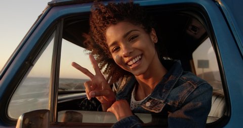 Front view close up of African american woman showing victory sign in pickup truck at beach. She is smiling and looking at camera 