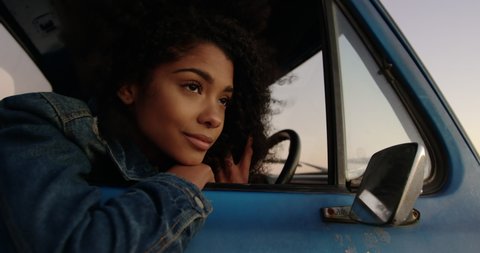 Front view close up of African american woman leaning on window of pickup truck at beach. She is thoughtful and looking away