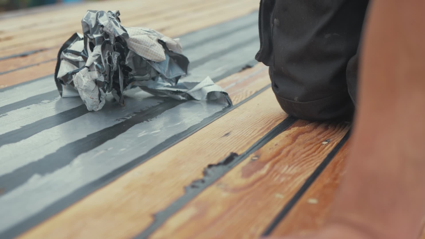 Man removes masking tape from sealed timber roof planking of wooden boat and balls it up.