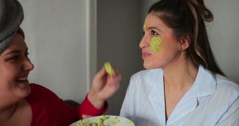 Close-up of a small group of female friends sitting indoors enjoying a girls night in, they are applying an avocado mask to a young adults face.