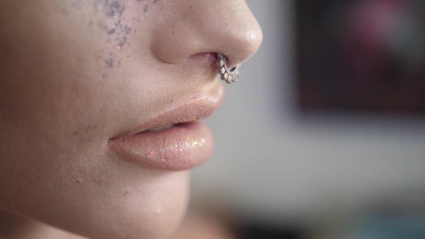 Extreme closeup of woman with nose ring smoking. Cigarette put between lips of lady sitting in her home.