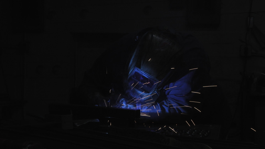 A welder creating bright blue sparks as they work on a project in a workshop