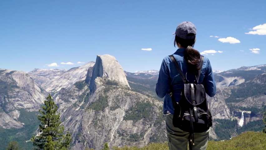 back view of japanese lady tourist on peak of high rocks in yosemite national park sightseeing half dome trail view with blue sky. Sport active life concept. relax woman backpacker on mountain top Royalty-Free Stock Footage #1031281277