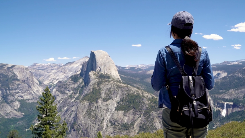 back view of japanese lady tourist on peak of high rocks in yosemite national park sightseeing half dome trail view with blue sky. Sport active life concept. relax woman backpacker on mountain top