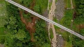 Aerial footage top view of suspension bridge crossing small river in green valley
