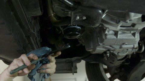 Garage workshop mechanic unscrews & removes old oil filter from car. Shot Pro Res at 200fps