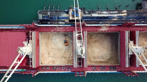 Large ship cranees containers into hold to off load shipment of sugar in harbor, Aerial View