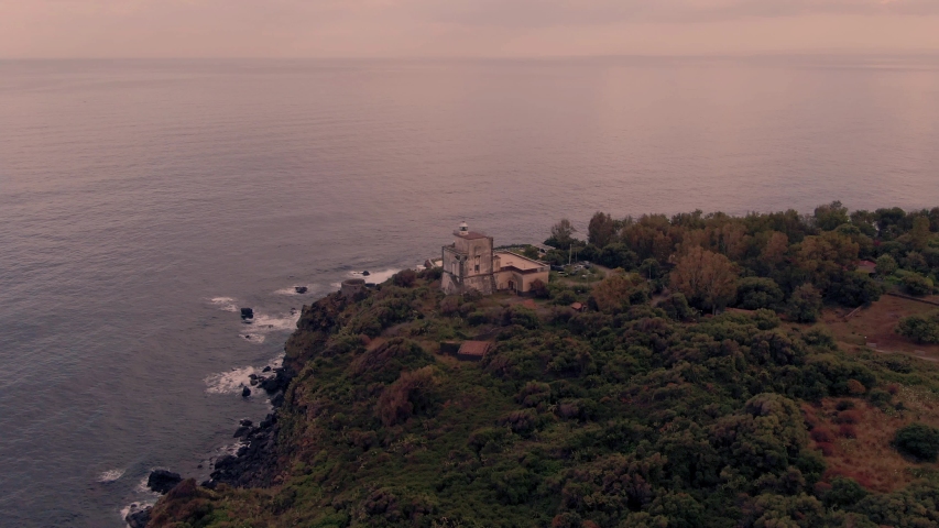 Aerial orbiting view of a lighthouse at sunset in the East coast of Sicily