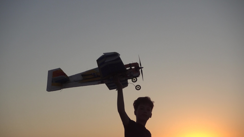 Child with a wooden plane against the sunset. Boy  silhouette Playing Outside With Toy Airplane