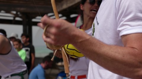 Haifa, Israel - June 8th 2019: Roda (Capoeira circle) at the beach promenade. Close up of hands playing the Berimbau. Woman singing and playing the Pandeiro in the background.