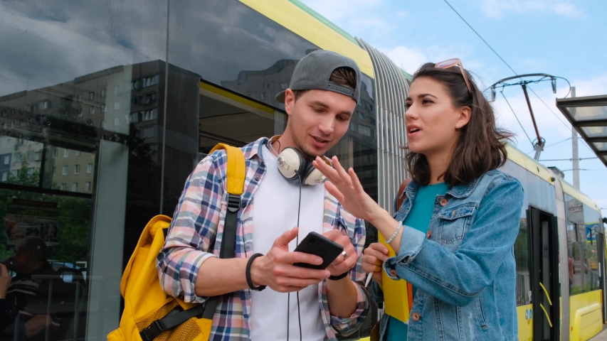 Smiling girl helping lost male tourist to find way. Lost tourist to find way. Background tram station.