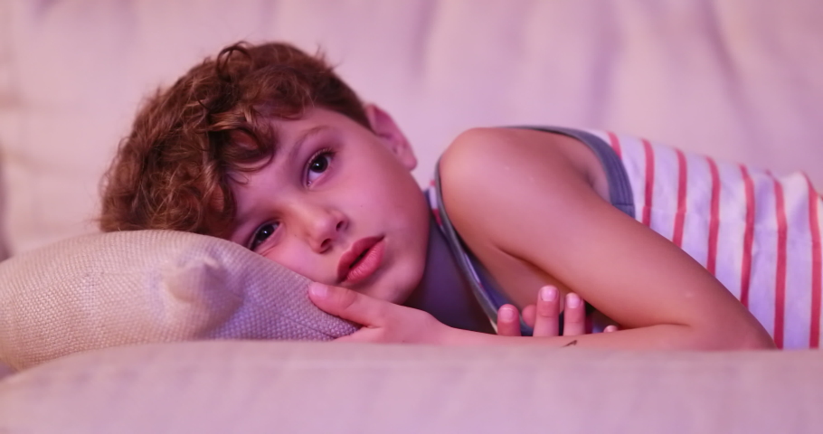 
Tired child young boy gradually falling asleep in living room sofa in the evening watching movie