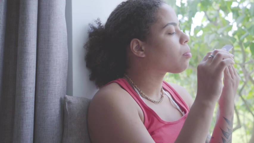 Portrait African American woman sitting on the window sill cutting nails with a nail file. The girl caring about herself. Happy girl relaxing at home. Day off of the lady