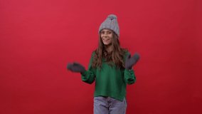 girl on a red background in a hat and gloves rejoices
