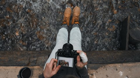 Feet in boots close-up. A woman sitting on a wooden bridge dangling his feet over a mountain river and takes them to the camera. Cozy coolness. Rear view, Slow motion, 4K