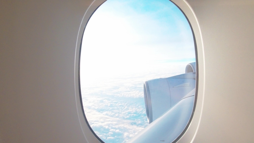 Visual of blue sky and white clouds zoom-in and zoom-out from inside airplane cabin window which handheld action camera move dolly in to glass frame to show beautiful atmosphere and sunlight outside