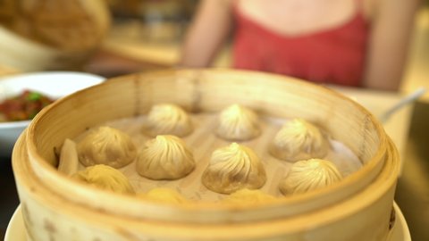 Asian cuisine. Woman eating typical shanghai chinese food xiao long bao soup filled dumplings at restaurant opening bamboo steamer steaming basket tray with hot fresh traditional handmade potstickers.