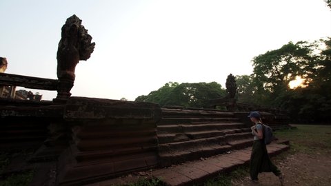 Woman tourist with backpack is going upstairs between two seven-headed naga statues in early morning at Angkor Wat temple. Cambodia